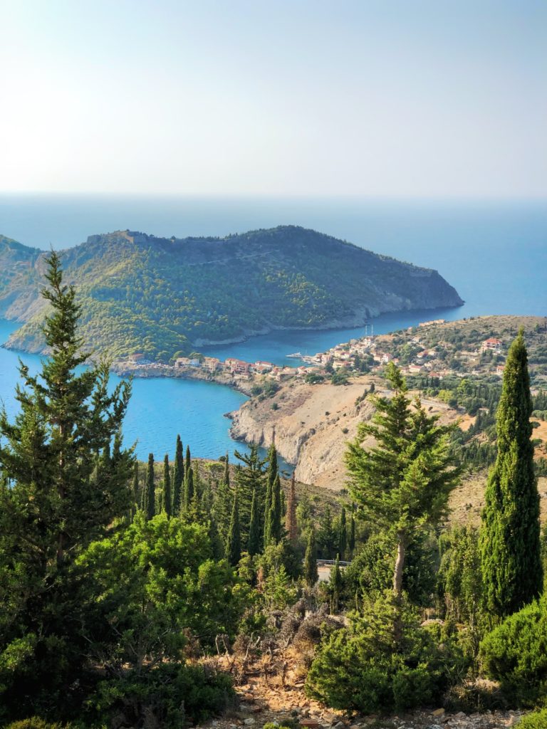 Scenic view from a hilltop looking down on Assos Kefalonia with crystal clear waters, surrounded by lush greenery and small village structures